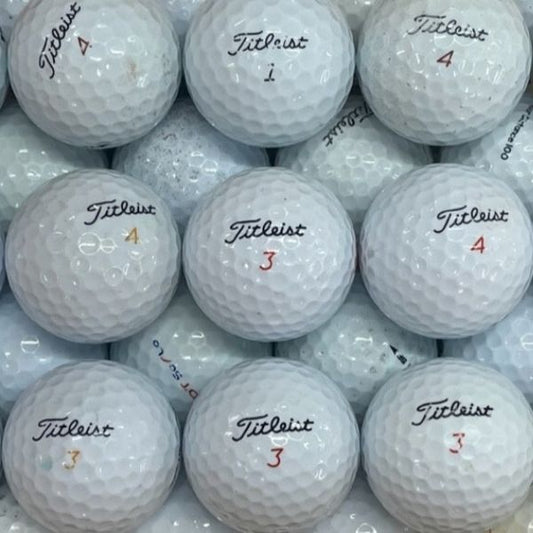 A close-up pile of white Titleist golf balls, with several visible in the center showing the black Titleist logo and red numbered markings.