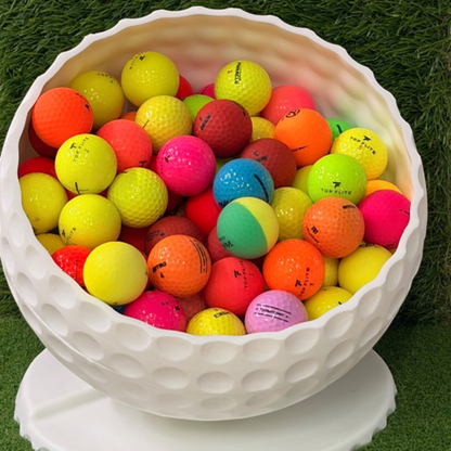 White bowl filled with multicolored golf balls on a grassy background